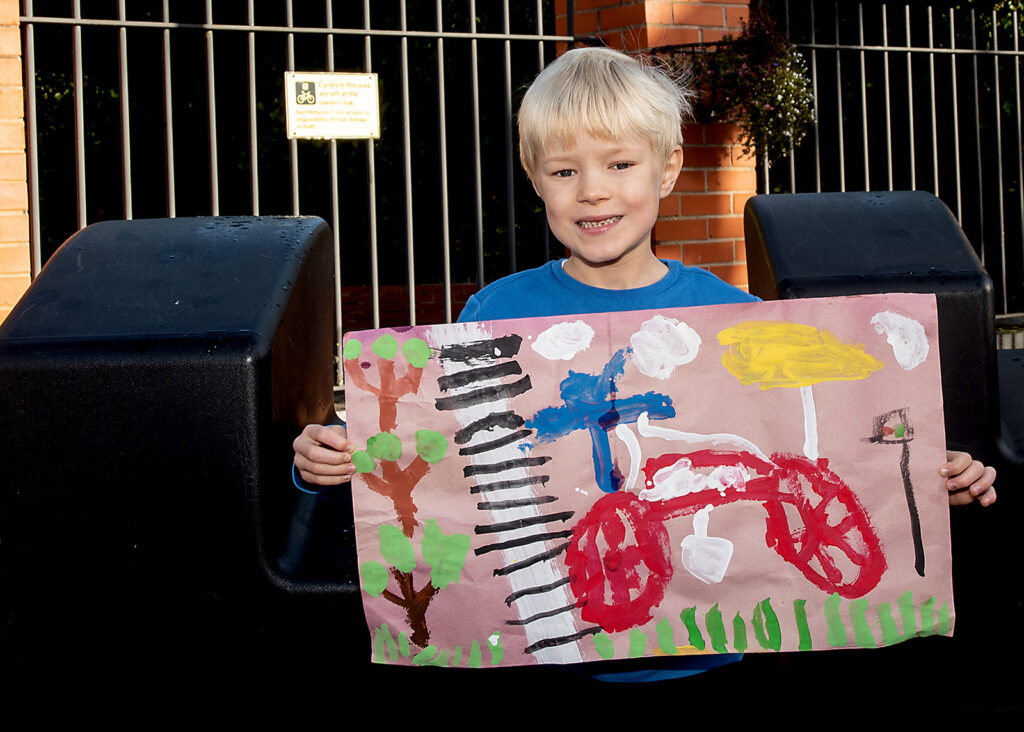 A small boy displaying his artwork at the side of the railway