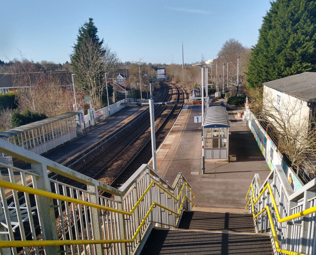 A view of Platform 1 at Uttoxeter station, taken from the top of the stairs on the footbridge. The platform is adorned with colourful designs.