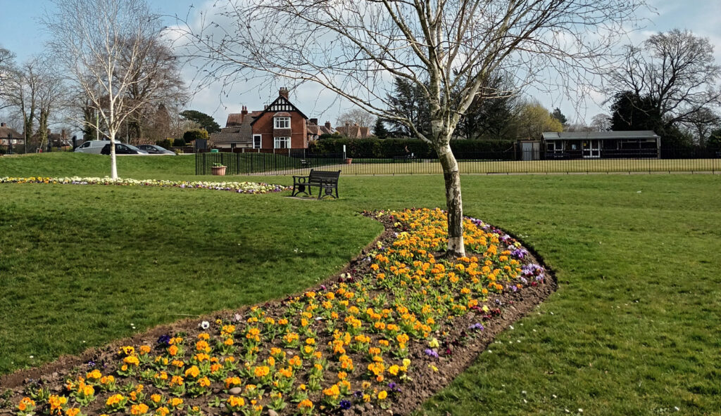 An image of Bramshall Road Park, an open grassy park space with multicoloured flowers and trees.