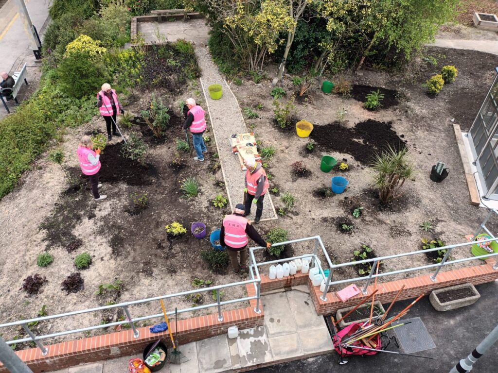 Picture taken from atop the new footbridge at Kidsgrove taken. Volunteers can be seen assisting with the garden renovations, digging holes and planting new shrubs.