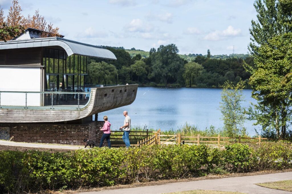 An image of the Westport Lake Visitor Center, situated on the edge of Westport Lake, a great spot for bird-watching and walking. It boasts a welcoming cafe with panoramic views of the water and is the perfect place to visit for families, walkers and nature lovers.