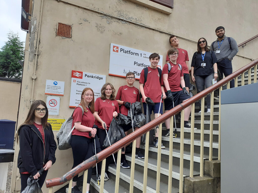 Picture of the Wolgarston High School students in front of Penkridge Station. They are all holding litter pickers and bags of rubbish.