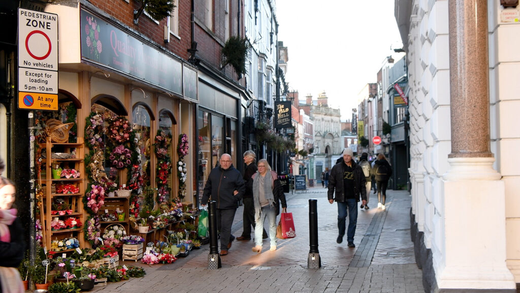 Shot of Derby Cathedral quarter. People can be seen walking past a colour flower shop, with shopping bags in hands.