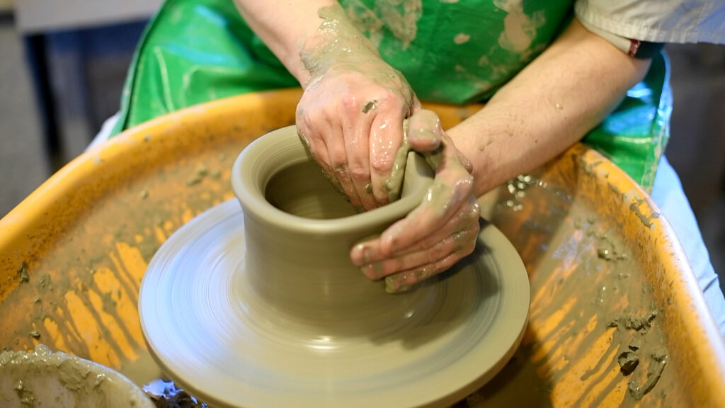 Picture of someone doing pottery at Gladstone Pottery Museum. They are shaping the clay into a vase.