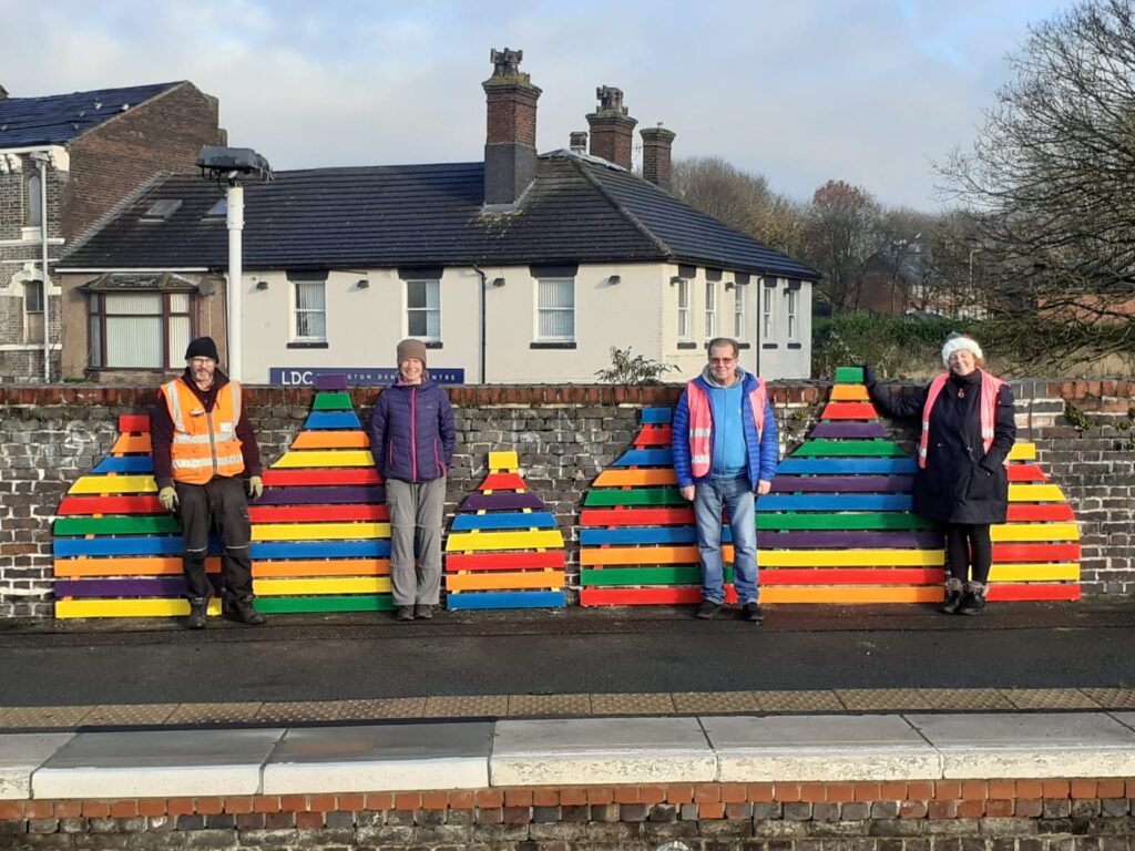 Station Volunteers pose next to the multi-coloured bottle kilns at Longton station